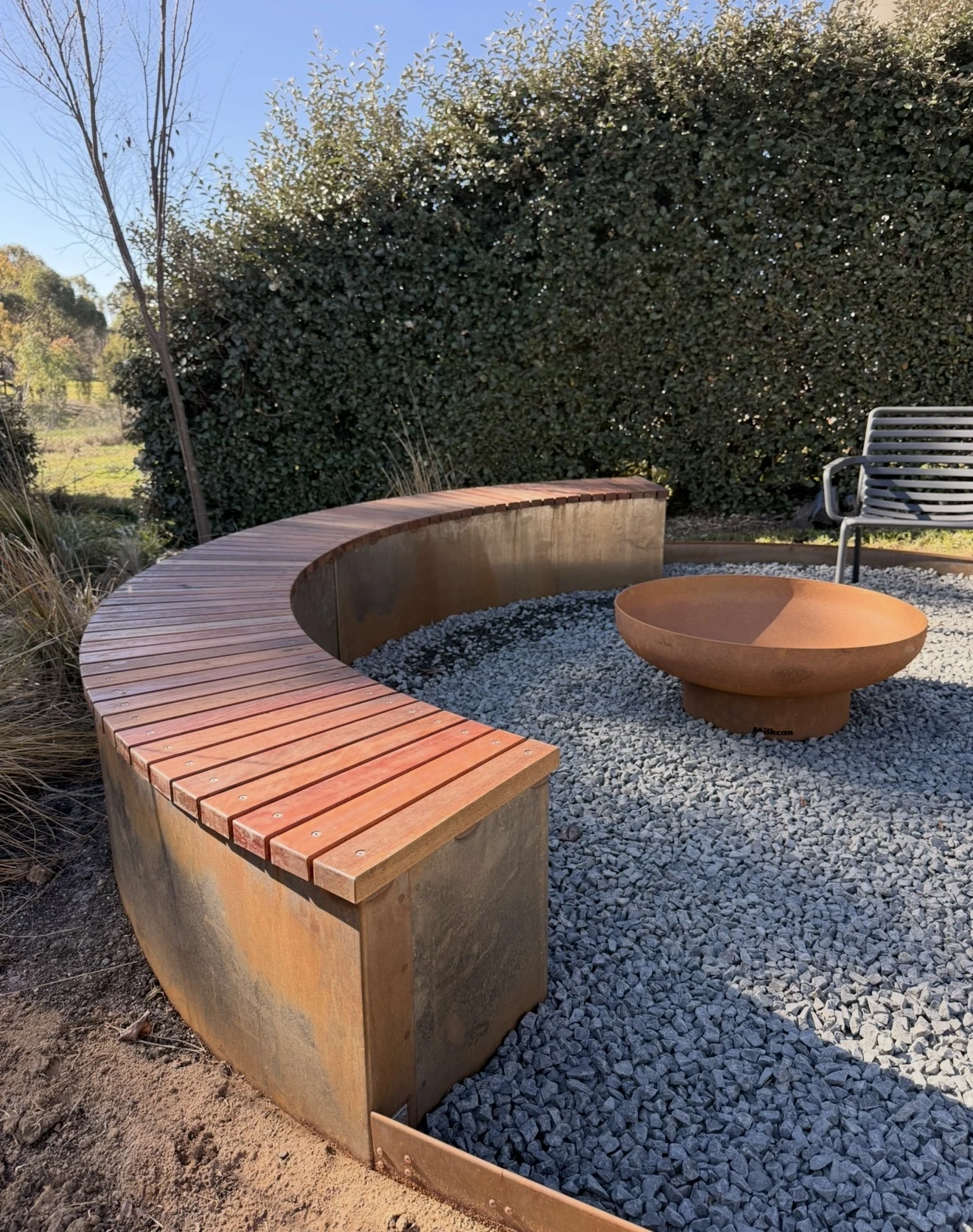 Curved timber seating on a weathering steel base around a fire pit
