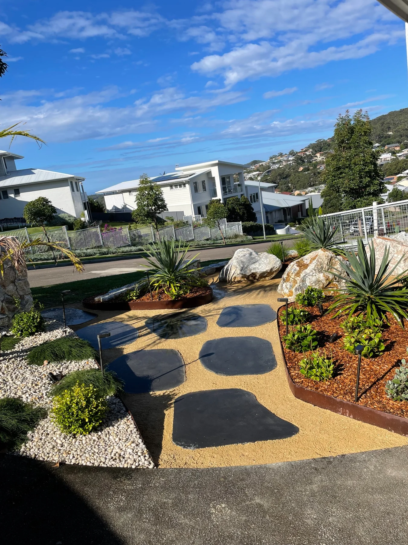 Sculpted stepping stones beside boulders and weathering steel garden edges