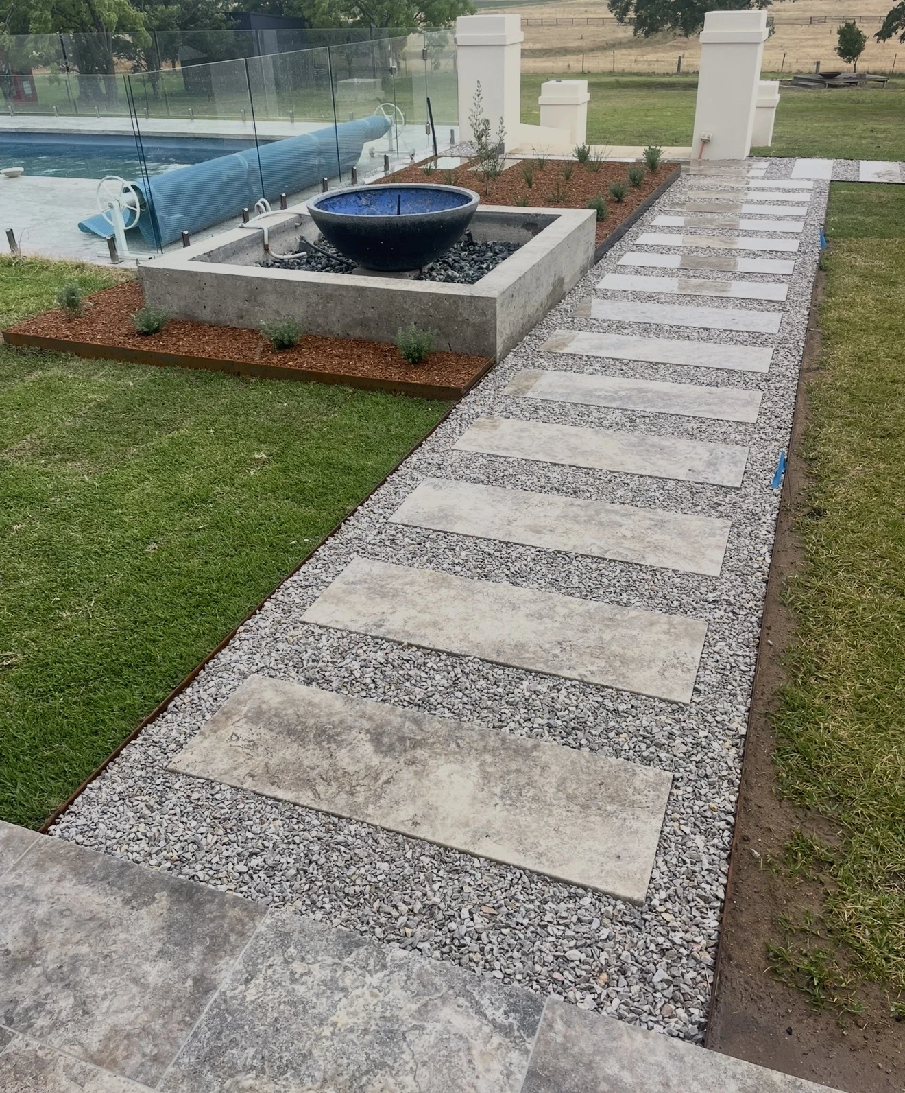 Stone stepping pathway alongside a constructed water feature and pool garden